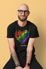 Load image into Gallery viewer, An gent with glasses wearing a black t-shirt. On the shirt is a heart made up of the AbleGamers logo, and came controller icons. The heart is colored in a rainbow, starting with Brown in the upper left to purple in the lower right. AbleGamers is at the bottom, and "GaymerX" on the sleeve