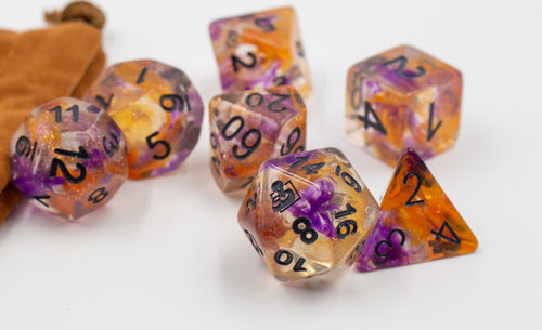 Close up of a clear set of dice with orange and purple swirled in. D20 with AbleGamers joystick logo. all the numbers are in black